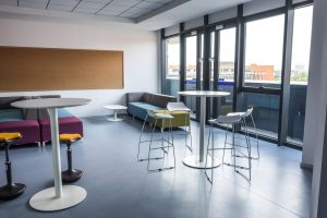 Salle de pause moderne dans une entreprise avec tables, fauteuils et espace café.