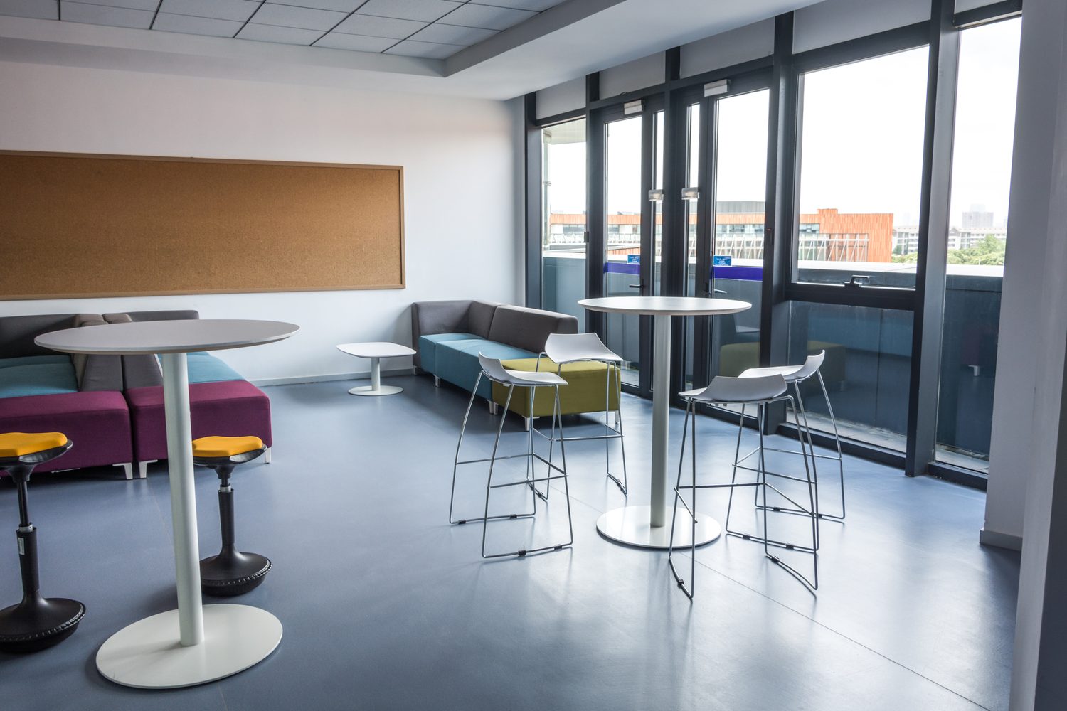 Salle de pause moderne dans une entreprise avec tables, fauteuils et espace café.